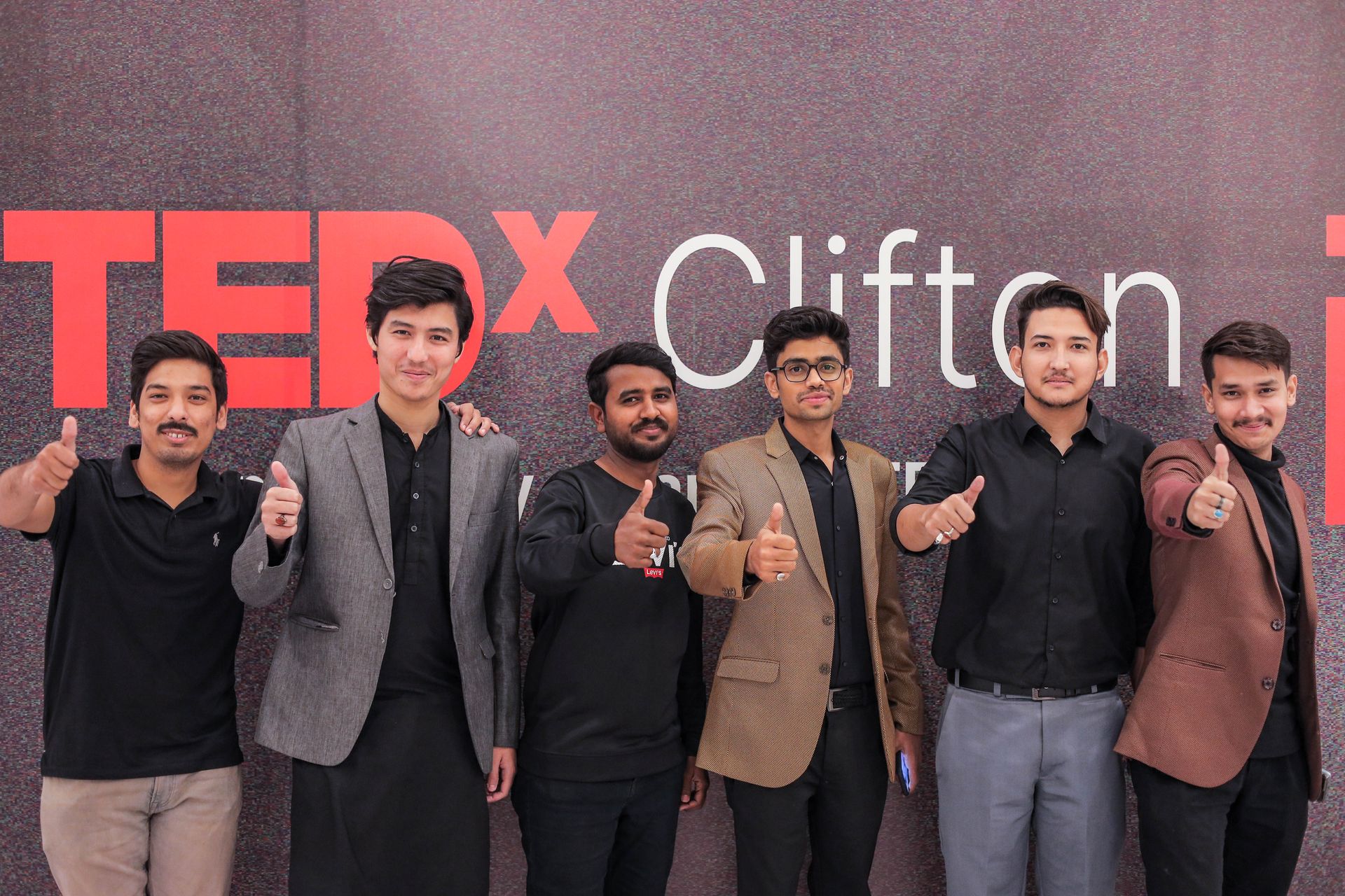 CoinConnect TEDx Clifton organizing team of six members in front of the iconic red TEDx Clifton signage, giving thumbs-up — lead organizing team
